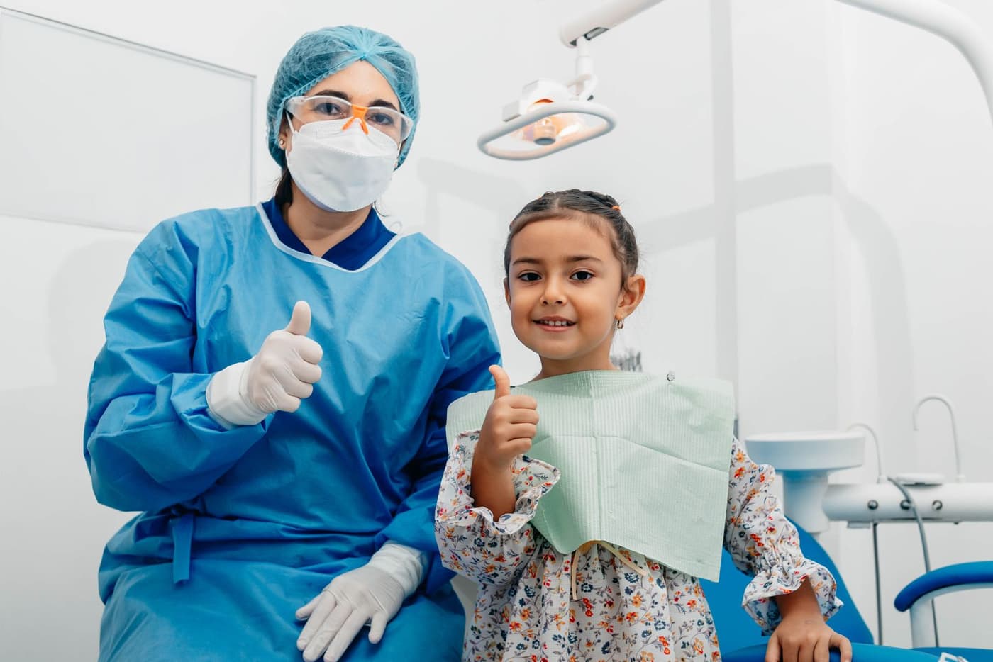 A dentist and a young patient smiling and giving a thumbs up in a dental office