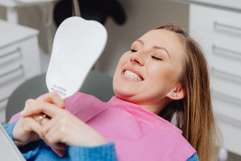 A patient smiling and holding up a hand mirror in the dental chair
